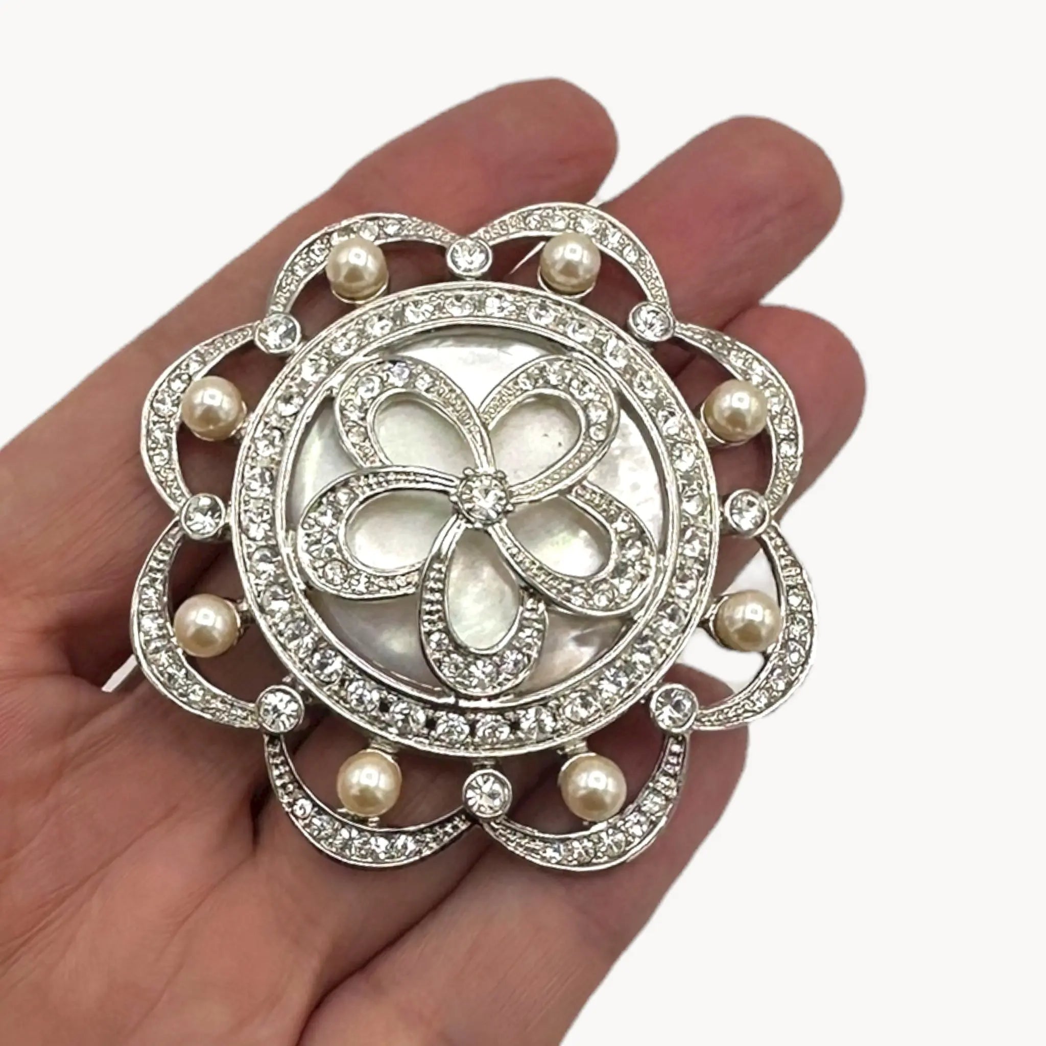 Shown on hand, Monet vintage silver tone brooch with rhinestones and faux pearls in floral design, elegant bridal jewelry piece on white background.