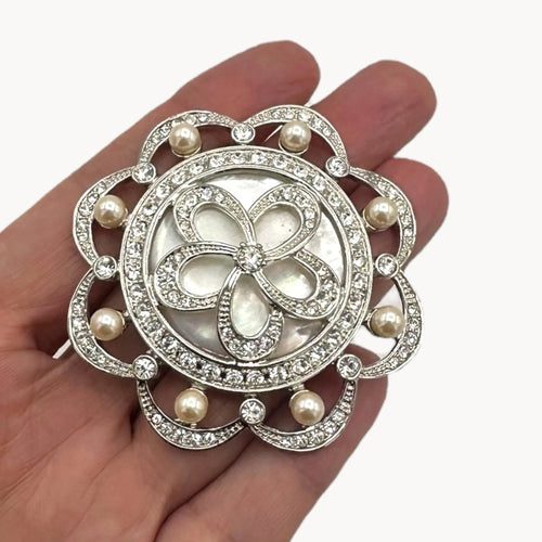 Shown on hand, Monet vintage silver tone brooch with rhinestones and faux pearls in floral design, elegant bridal jewelry piece on white background.