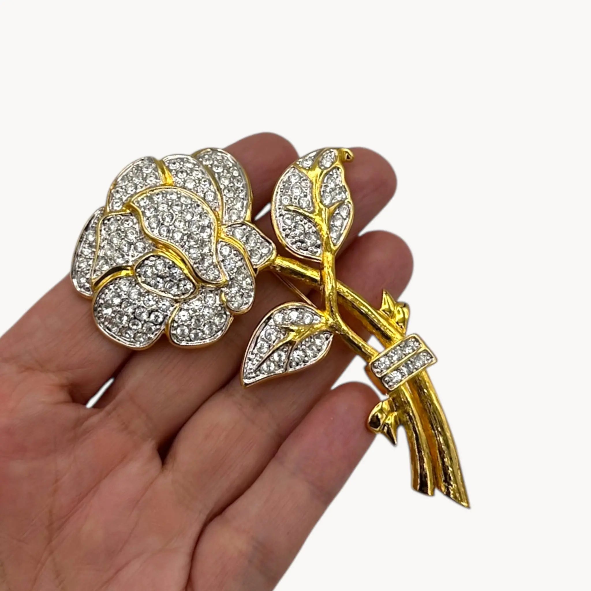 Scale size view of Nolan Miller gold and rhinestone flower brooch with pavé crystal accents