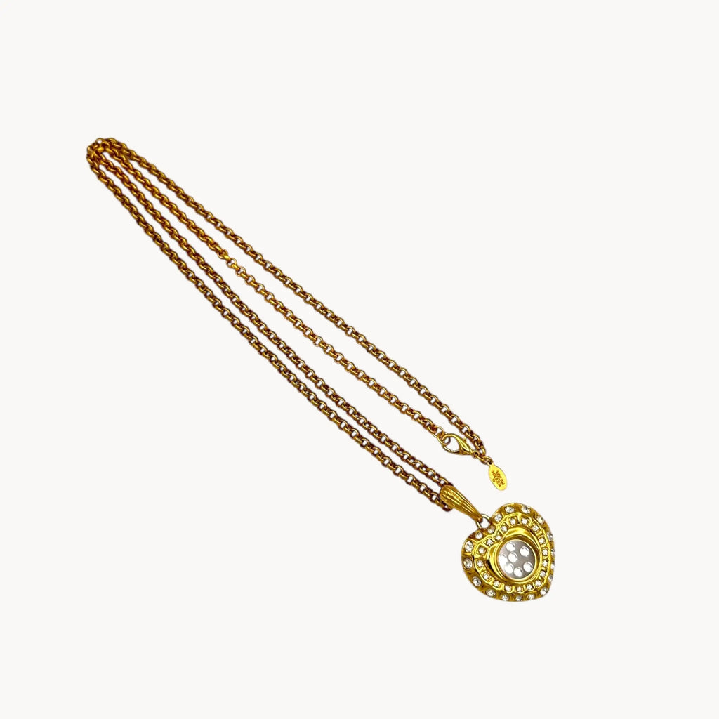 Nolan Miller gold-tone heart pendant necklace with clear rhinestones on long chain on white background.