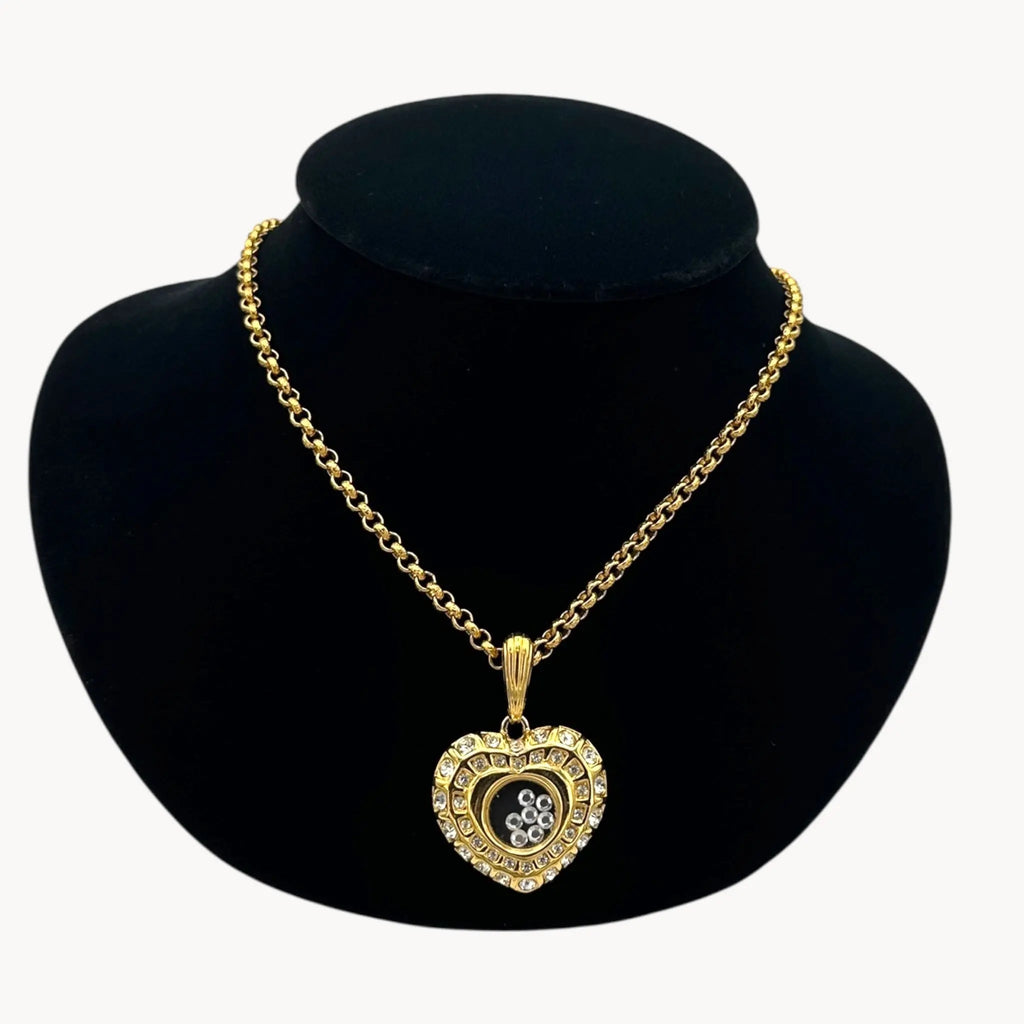 Close up view of Nolan Miller gold-tone heart pendant necklace with clear rhinestones on long chain on black bust.