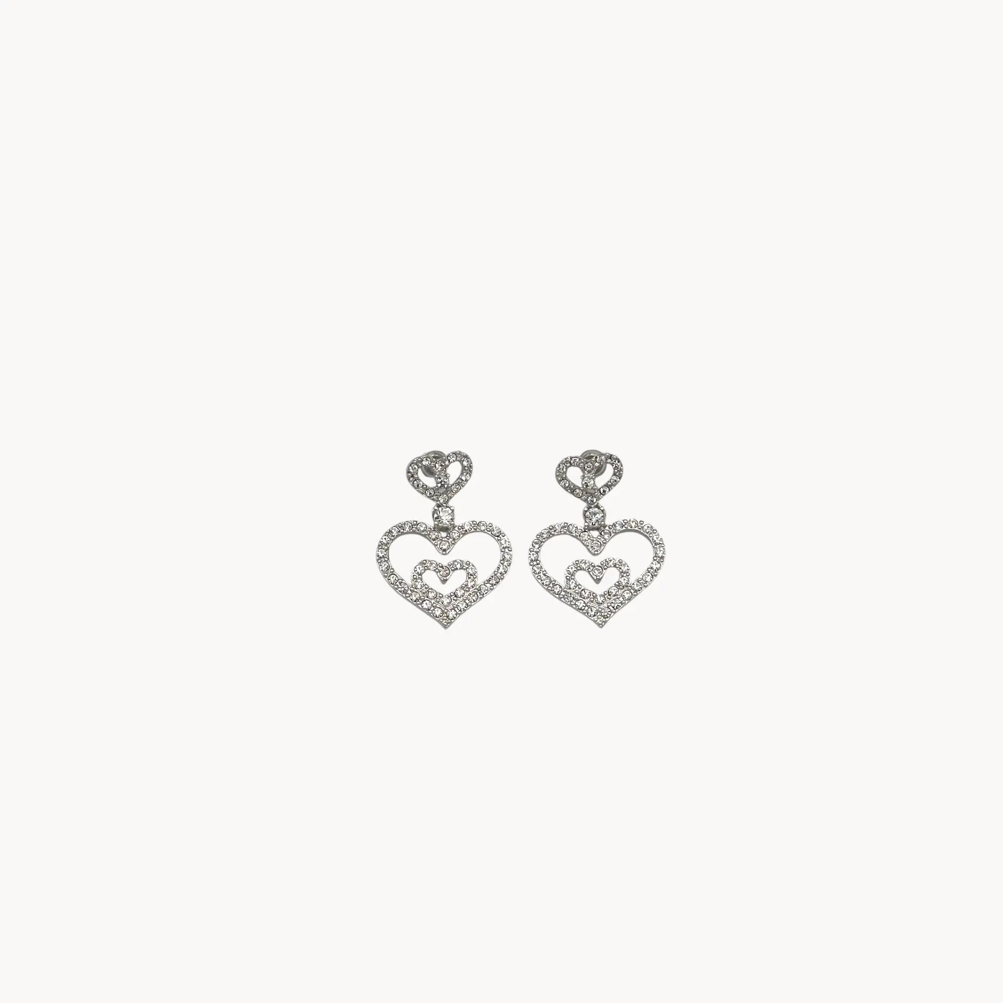 Close up view Vintage Nolan Miller rhinestone heart dangle pierced earrings with double open-heart design.