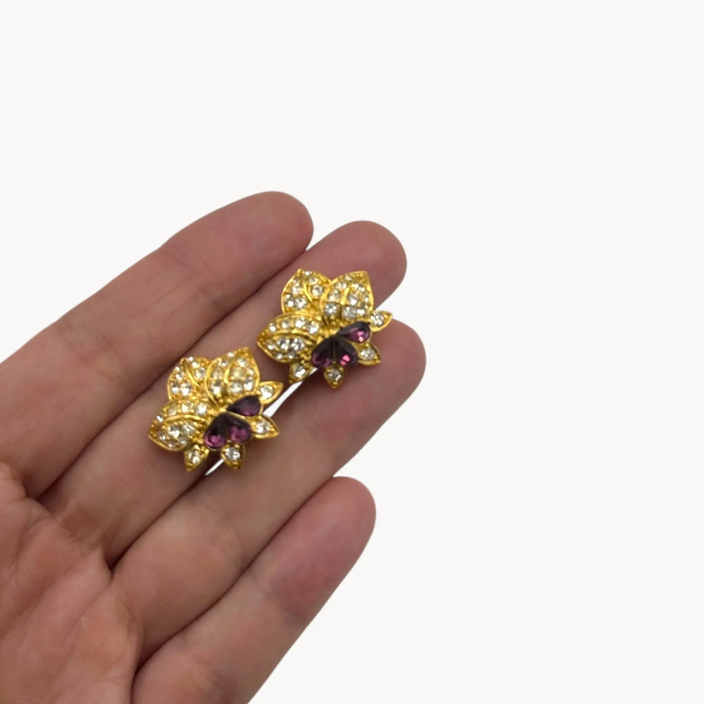 scale view of Nolan Miller vintage flower clip-on earrings with clear and amethyst rhinestones accents in gold-tone metal.