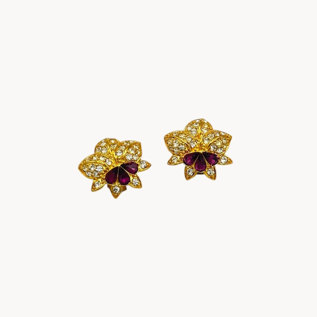 Close up view of Nolan Miller vintage flower clip-on earrings with clear and amethyst rhinestones accents in gold-tone metal.