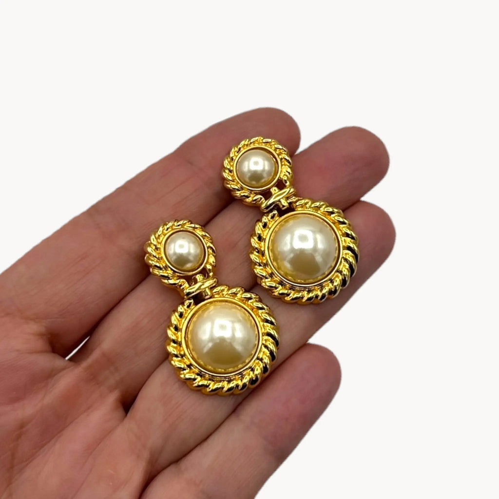 Vintage Paquette gold rope dangle earrings with faux pearls on hand on white background.