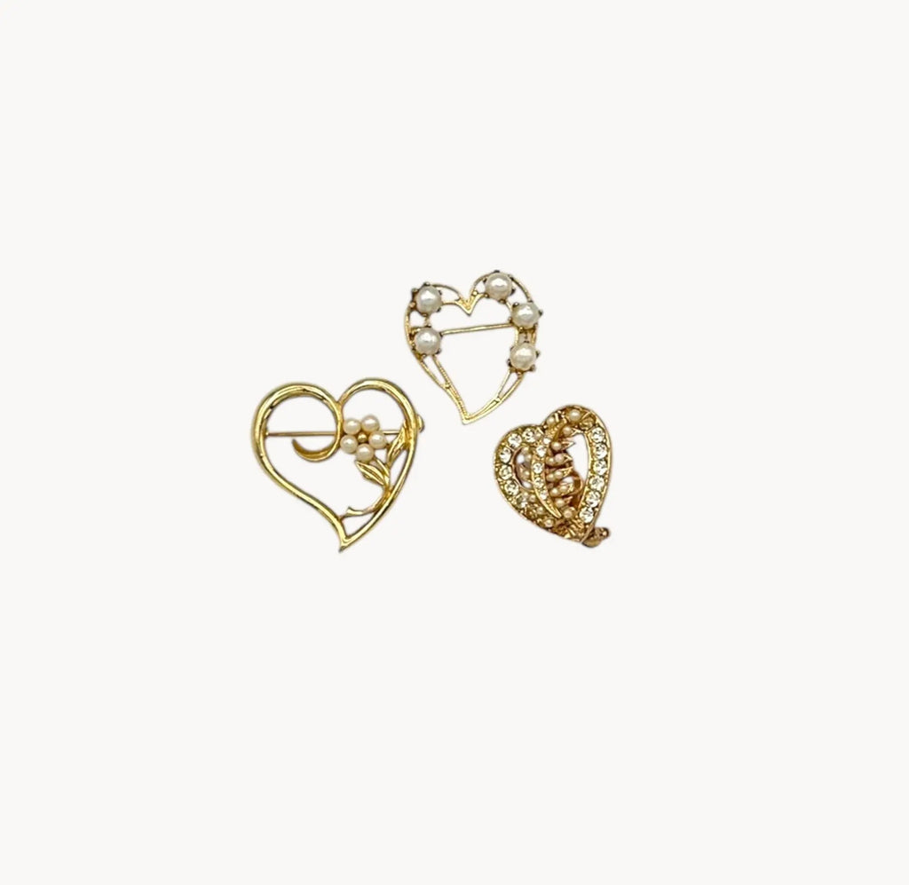 Set of three vintage gold heart brooches with pearls and rhinestones, mid-century scatter pins on white background.