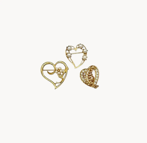 Set of three vintage gold heart brooches with pearls and rhinestones, mid-century scatter pins on white background.