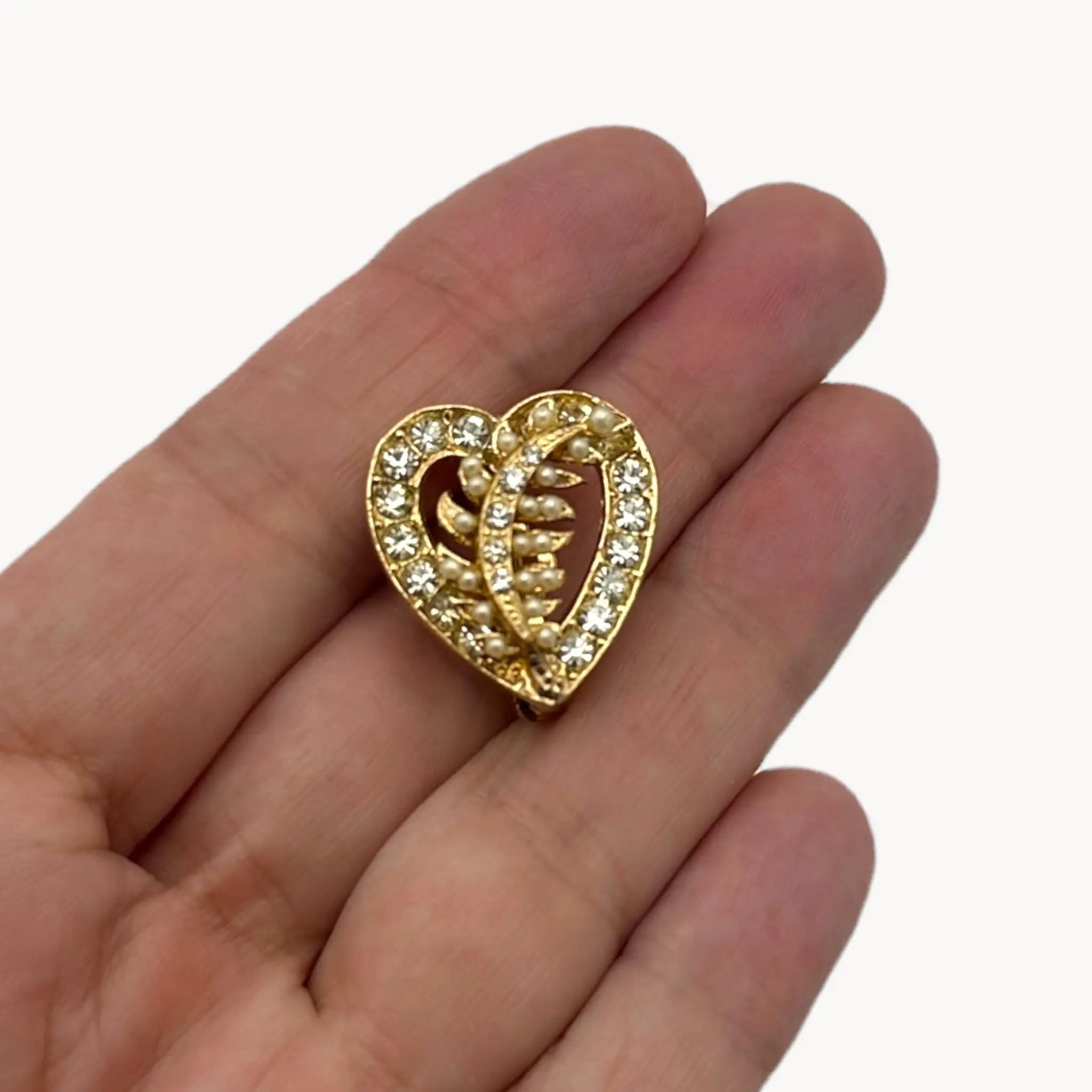 Vintage gold heart brooch with faux pearls and rhinestones on hand and white background.