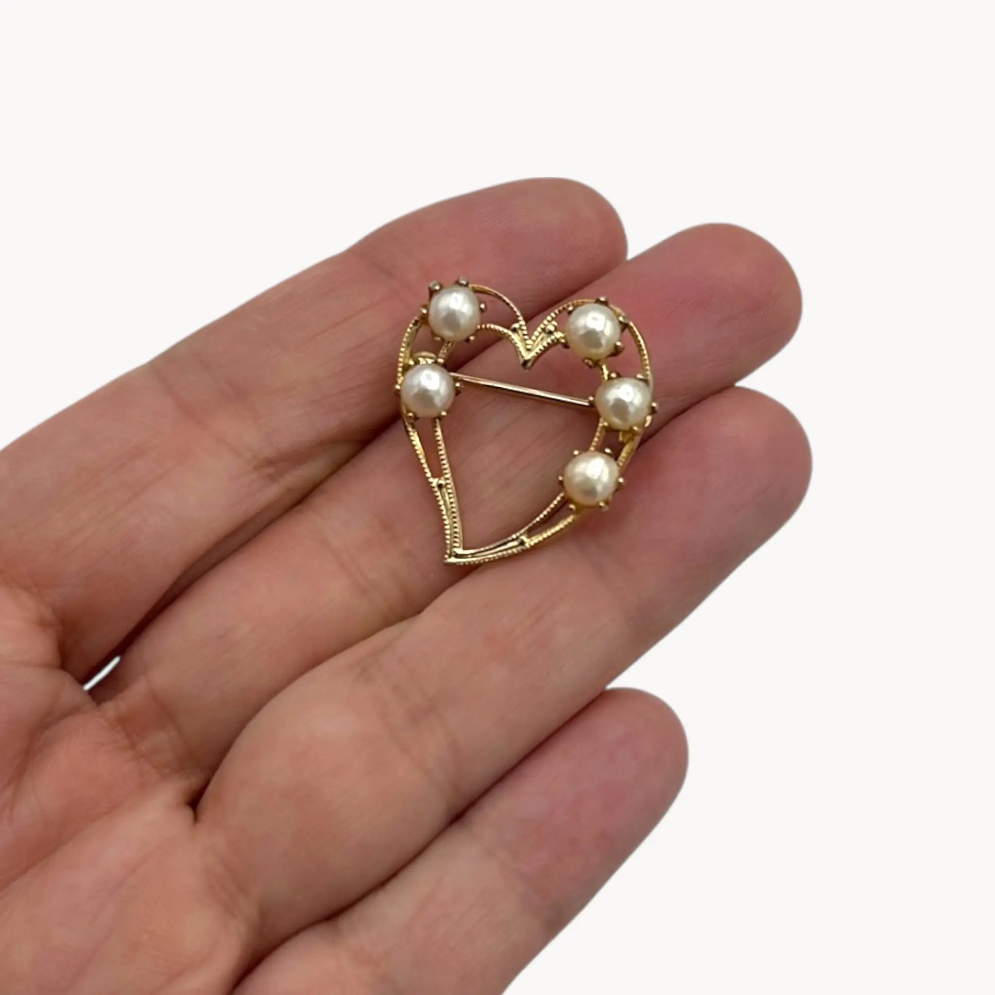 Vintage gold heart brooch with faux pearls on hand and white background.