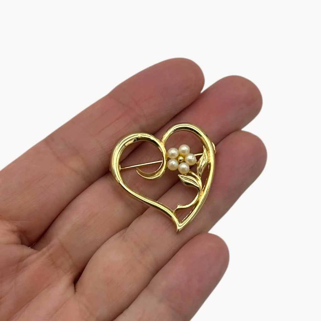 Vintage gold heart floral brooch with faux pearls on hand and white background.