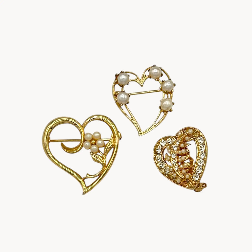 Close up of Set of three vintage gold heart brooches with pearls and rhinestones, mid-century scatter pins on white background.