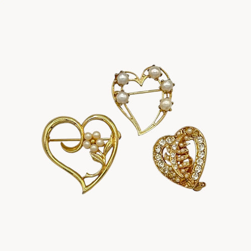 Close up of Set of three vintage gold heart brooches with pearls and rhinestones, mid-century scatter pins on white background.