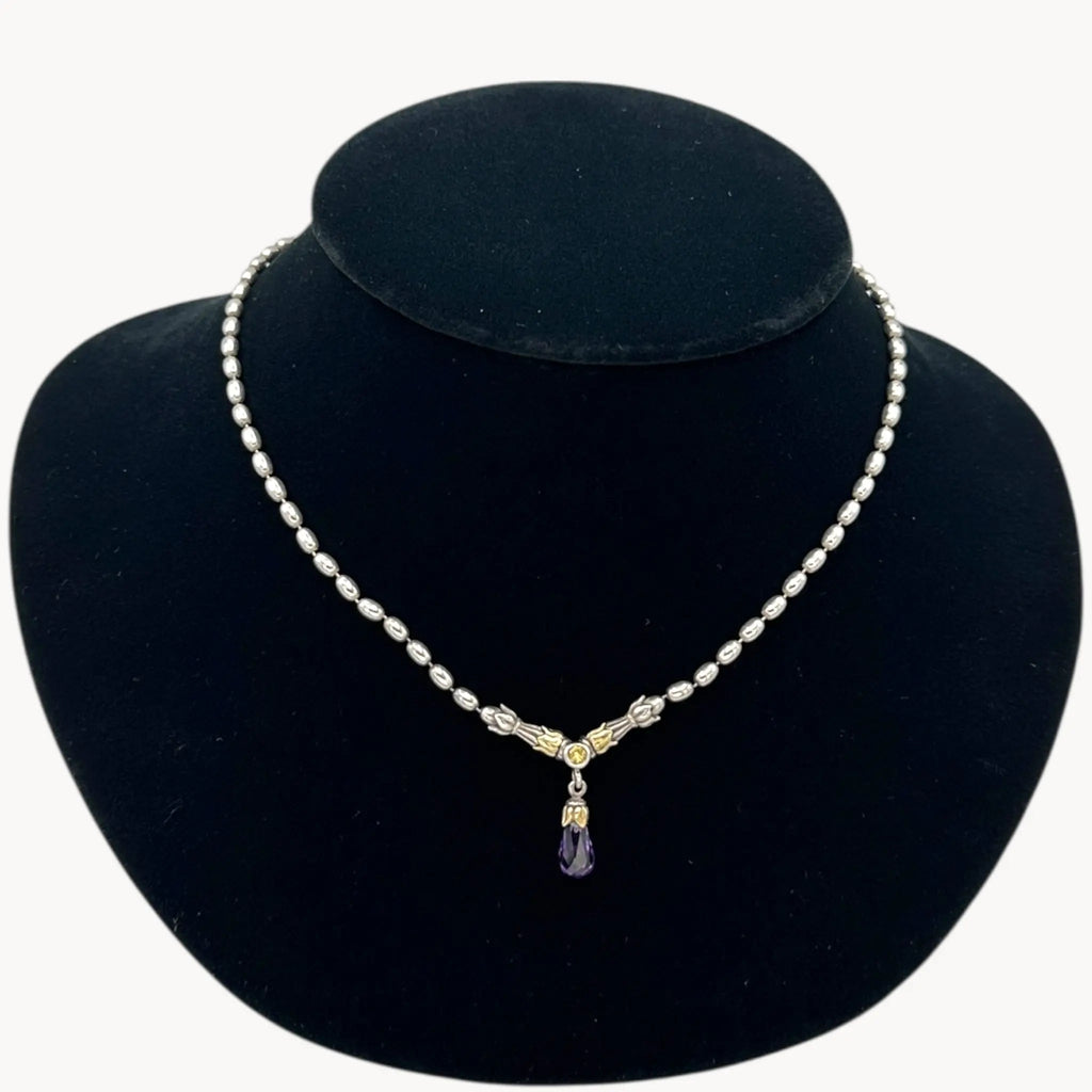 Close up view of Sterling silver and 14K yellow gold necklace with amethyst teardrop pendant on black bust.