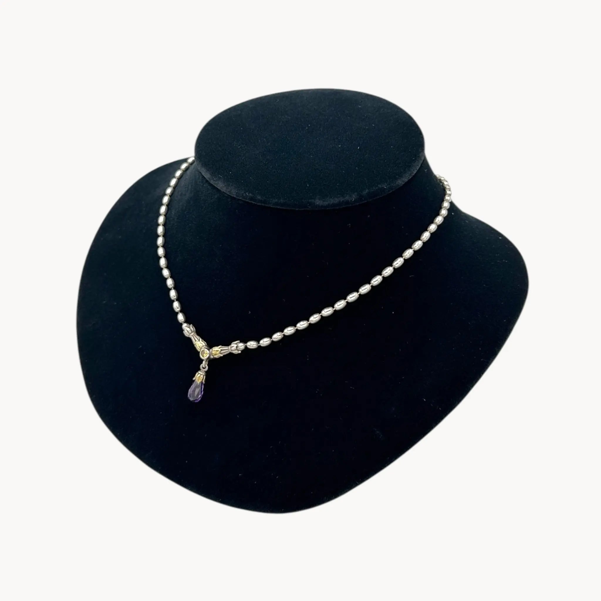 Close up side view of Sterling silver and 14K yellow gold necklace with amethyst teardrop pendant on black bust.