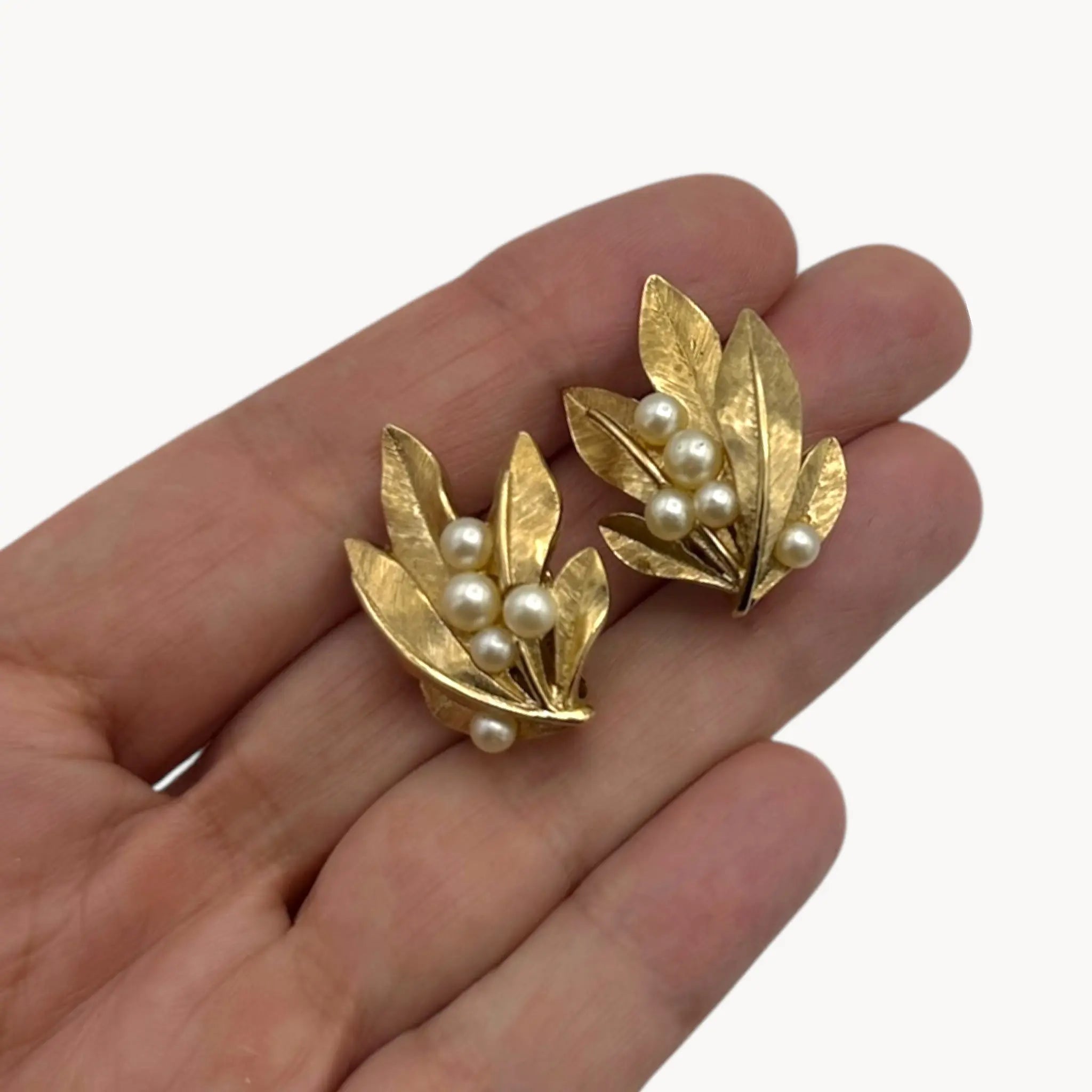 Scale size view on hand of Vintage Trifari gold leaf clip-on earrings with faux pearls, 1960s jewelry on white background.
