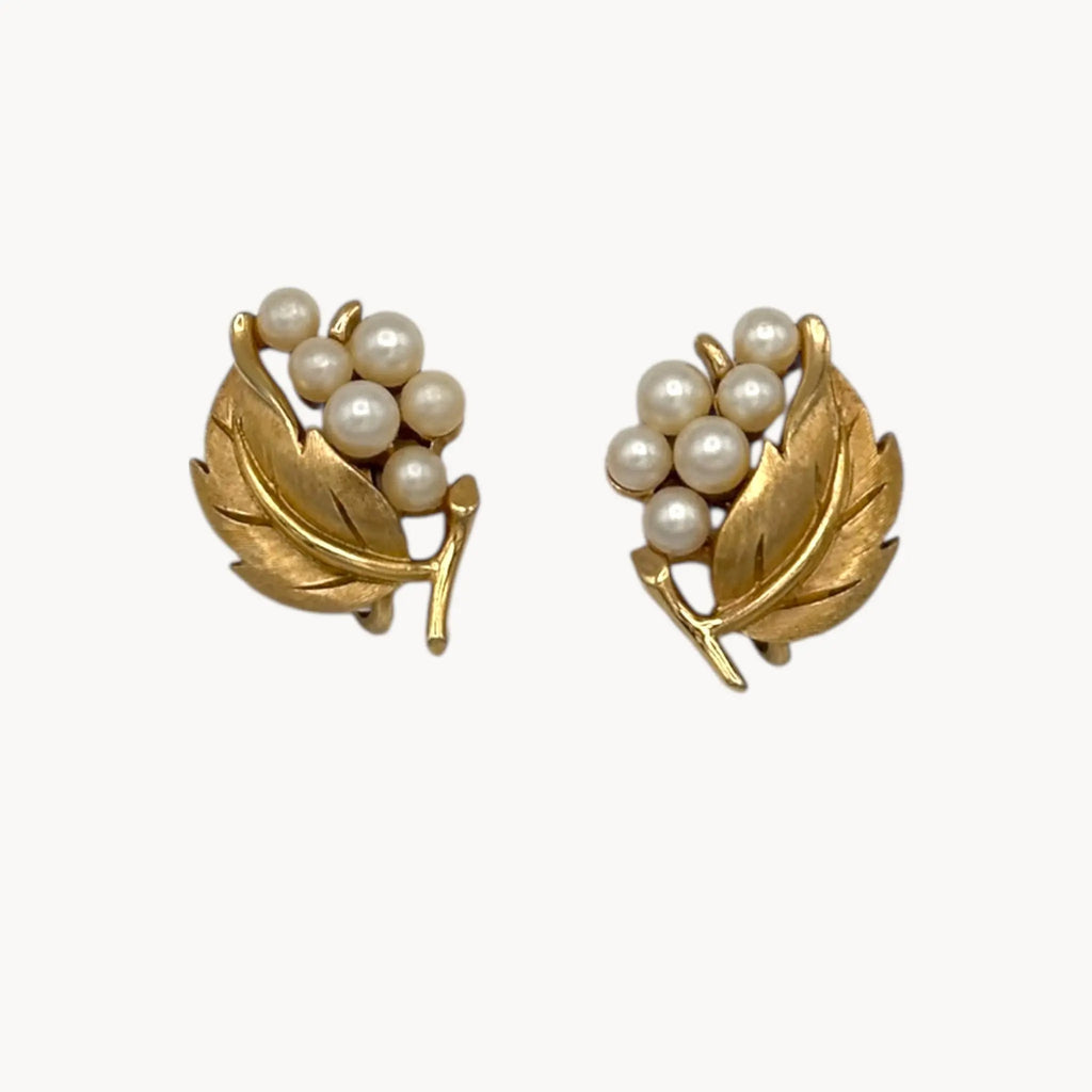 Close up view of Vintage Trifari gold leaf clip-on earrings with faux pearl clusters, mid-century jewelry on white back background.