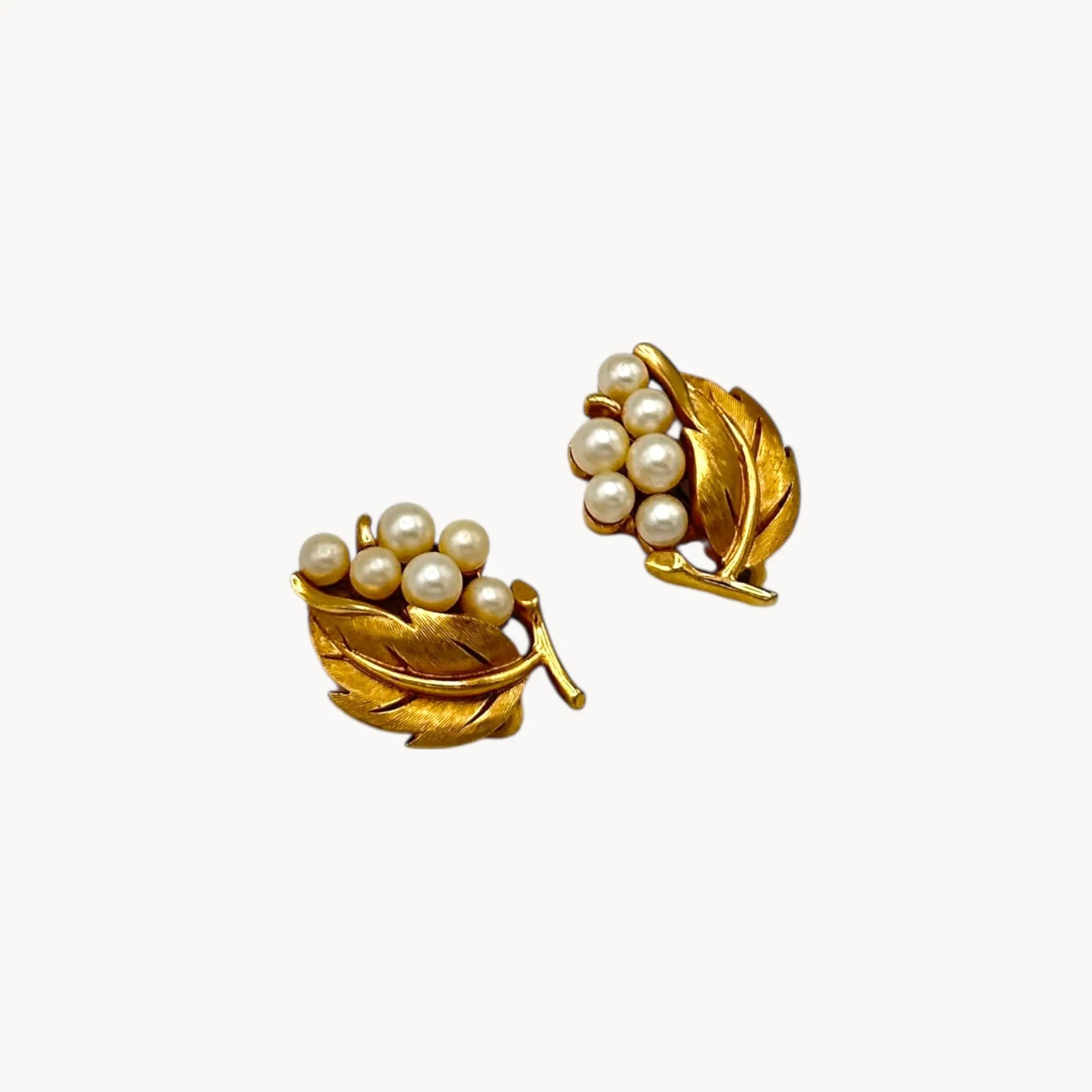 Side view of Vintage Trifari gold leaf clip-on earrings with faux pearl clusters, mid-century jewelry on white back background.