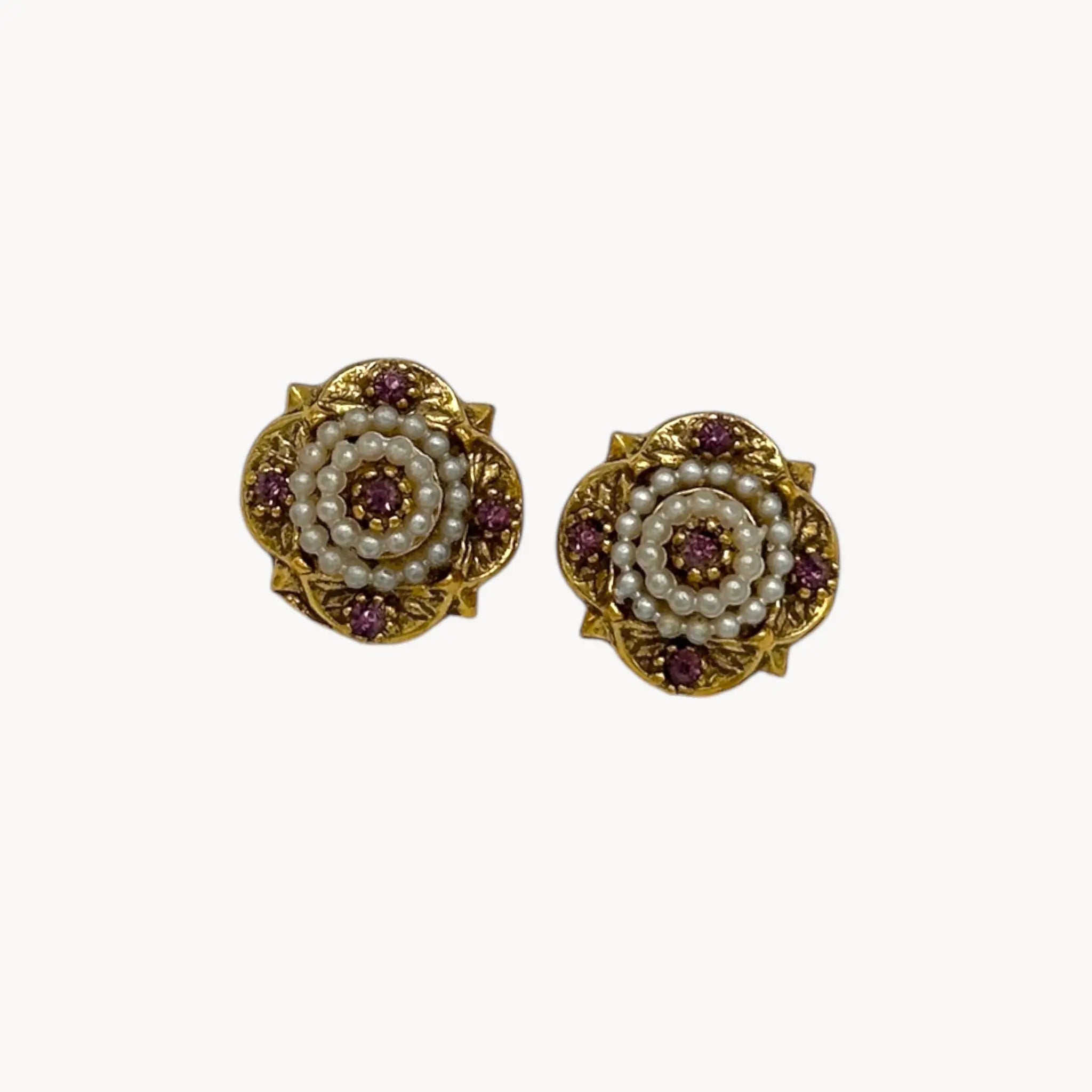 Close up view of Victorian revival gold clip-on earrings with faux pearls and purple rhinestones.