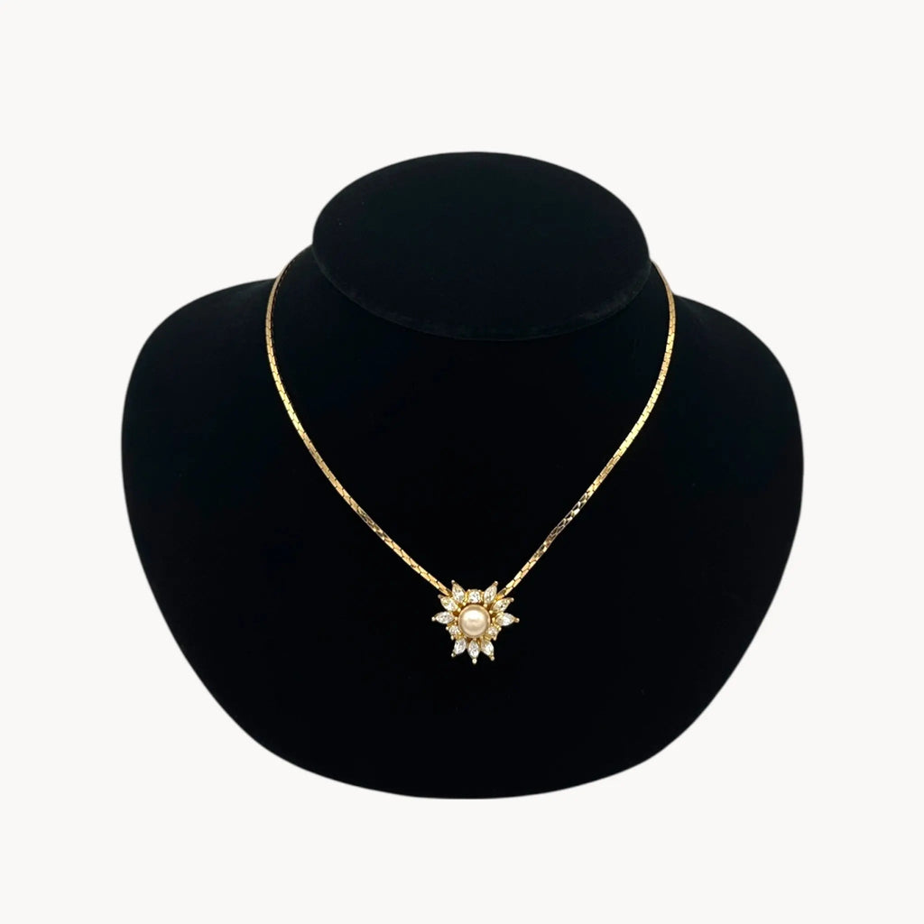 Close view Vintage Christian Dior necklace with gold-tone chain and starburst pendant featuring pearl center and crystal accents, 1980s bridal jewelry.