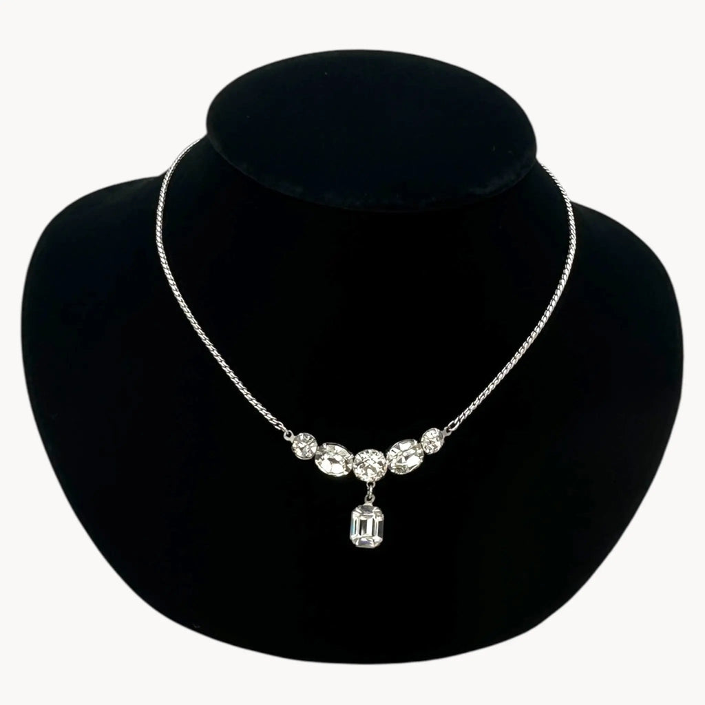 Close up view of Vintage rhinestone pendant necklace with round and emerald-cut stones on black bust.