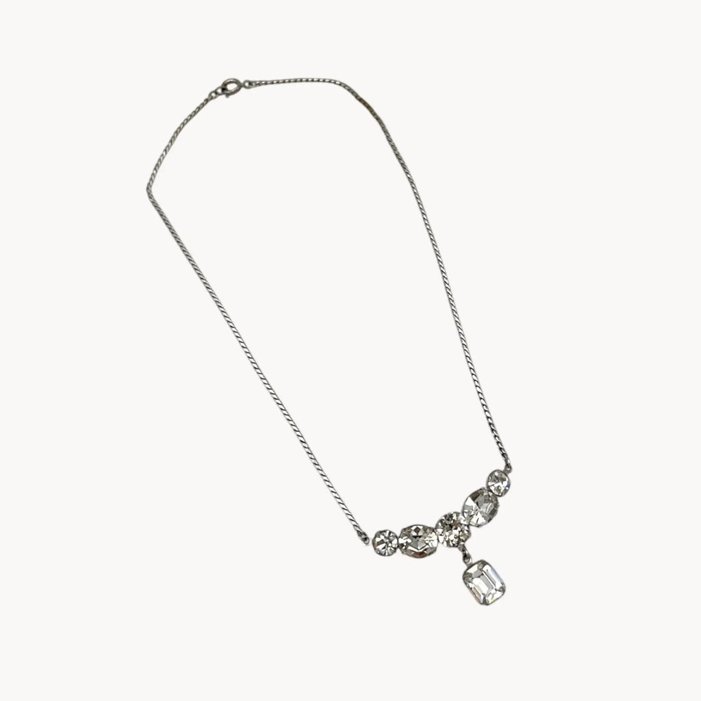 Close up view of Vintage rhinestone pendant necklace with round and emerald-cut stones on white background.