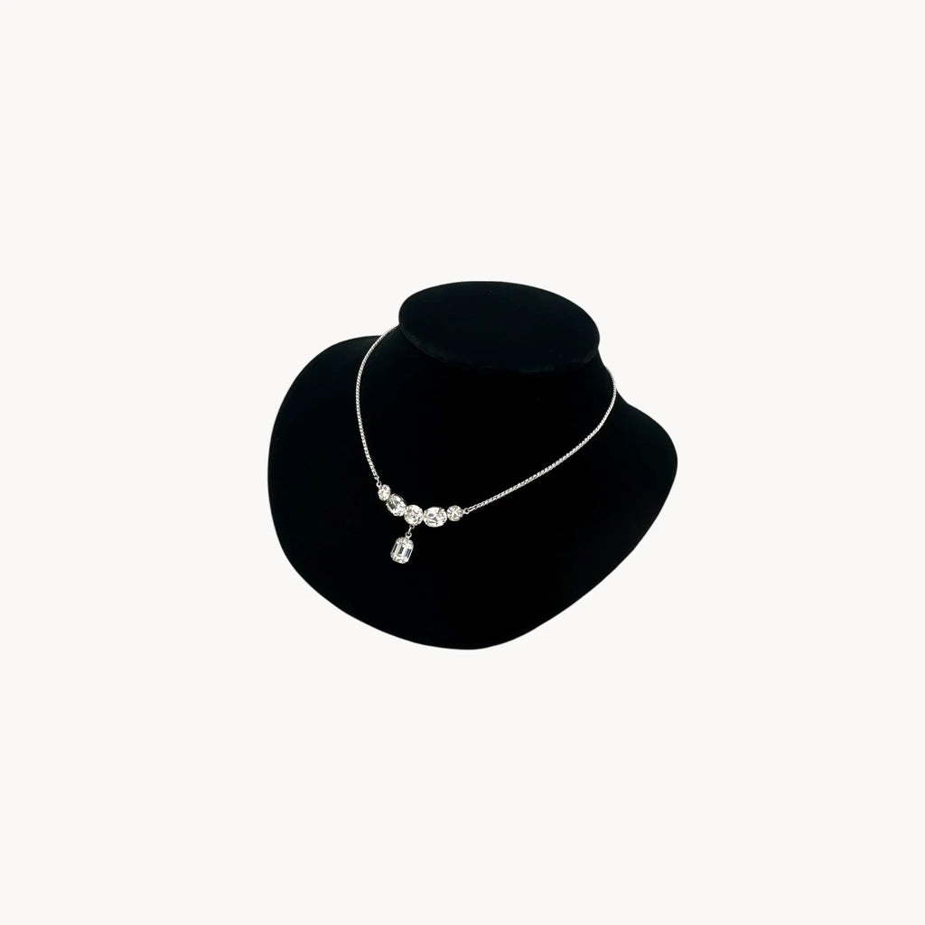 Side view of Vintage rhinestone pendant necklace with round and emerald-cut stones on black bust.