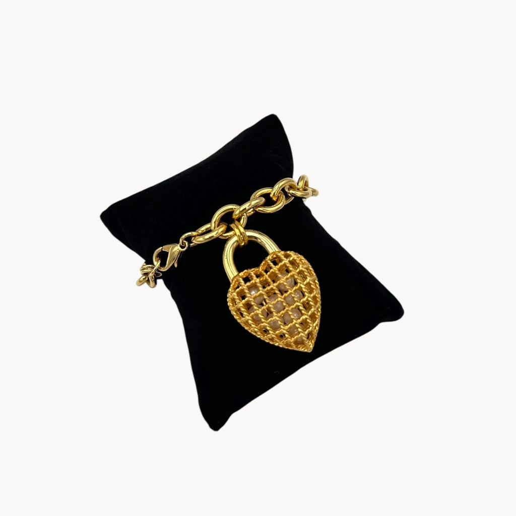 Bracelet on black pillow of Vintage gold caged pearl heart bracelet and matching clip-on earrings set, 1980s–1990s jewelry on white background.