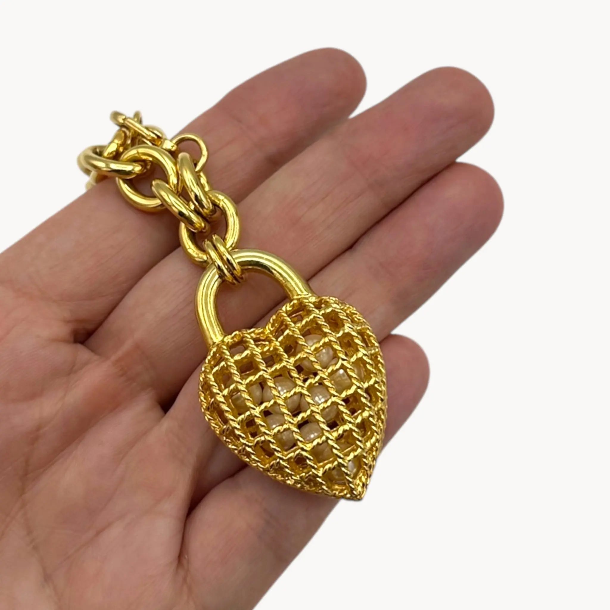 Bracelet charm close up of Vintage gold caged pearl heart bracelet and matching clip-on earrings set, 1980s–1990s jewelry on white background.