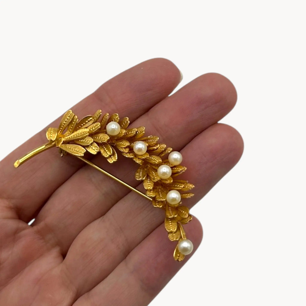 Scale size view on hand of Vintage gold-filled floral brooch with detailed leaf design and real pearl accents, mid-century shown on white background.