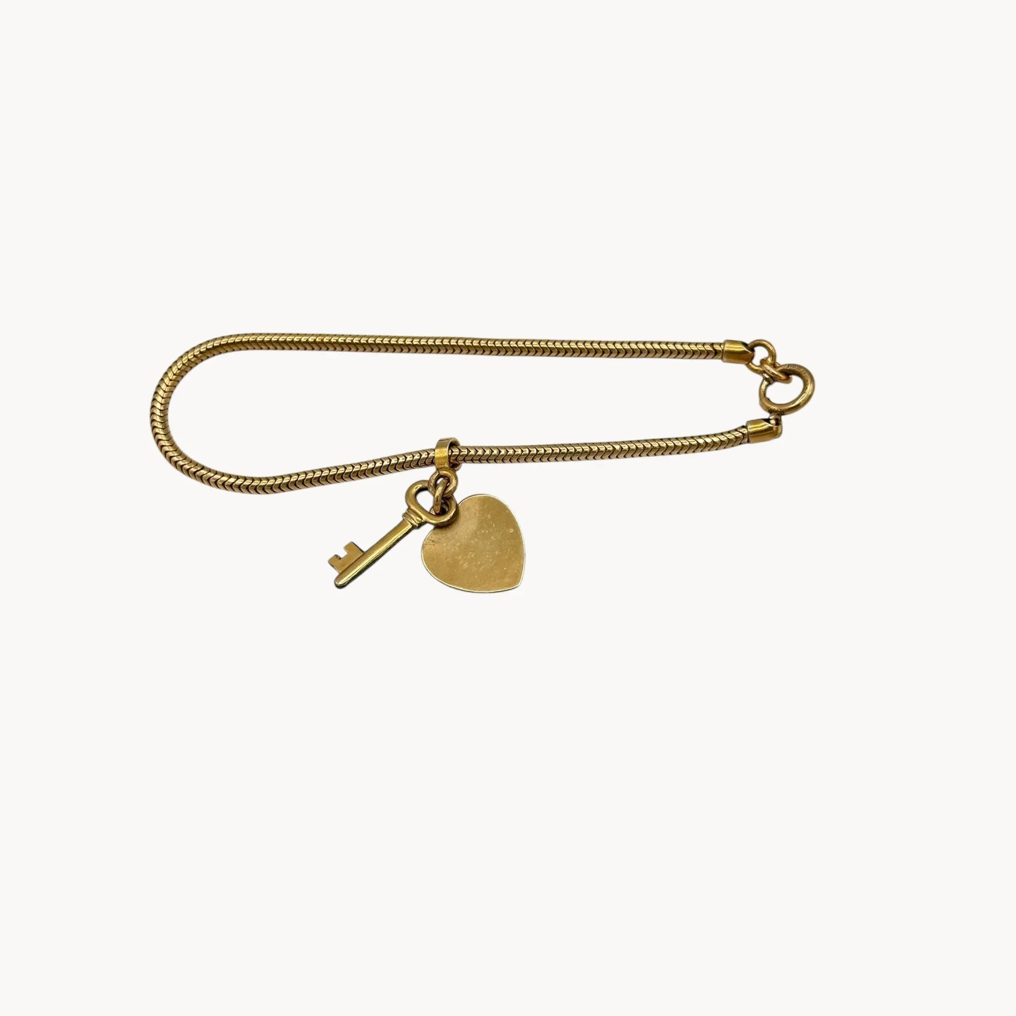 Against white background view of Vintage gold-filled snake link bracelet with sliding heart and key charm, romantic mid-century jewelry.