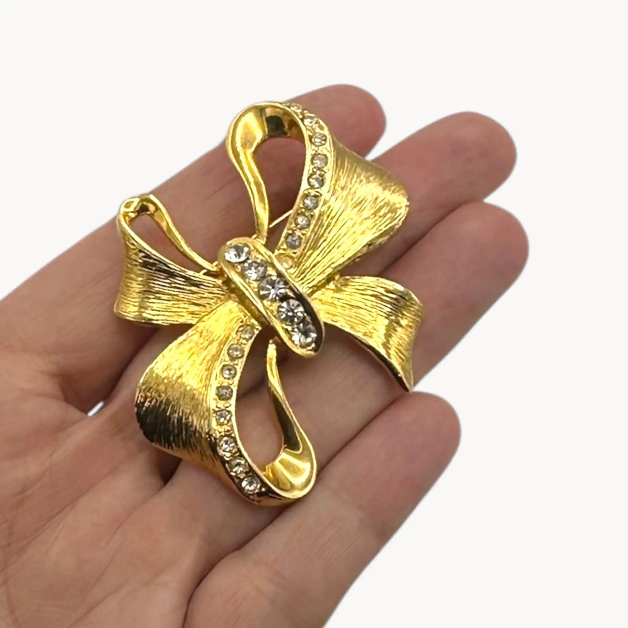 Gold bow-shaped brooch with rhinestones held in a hand on a white background