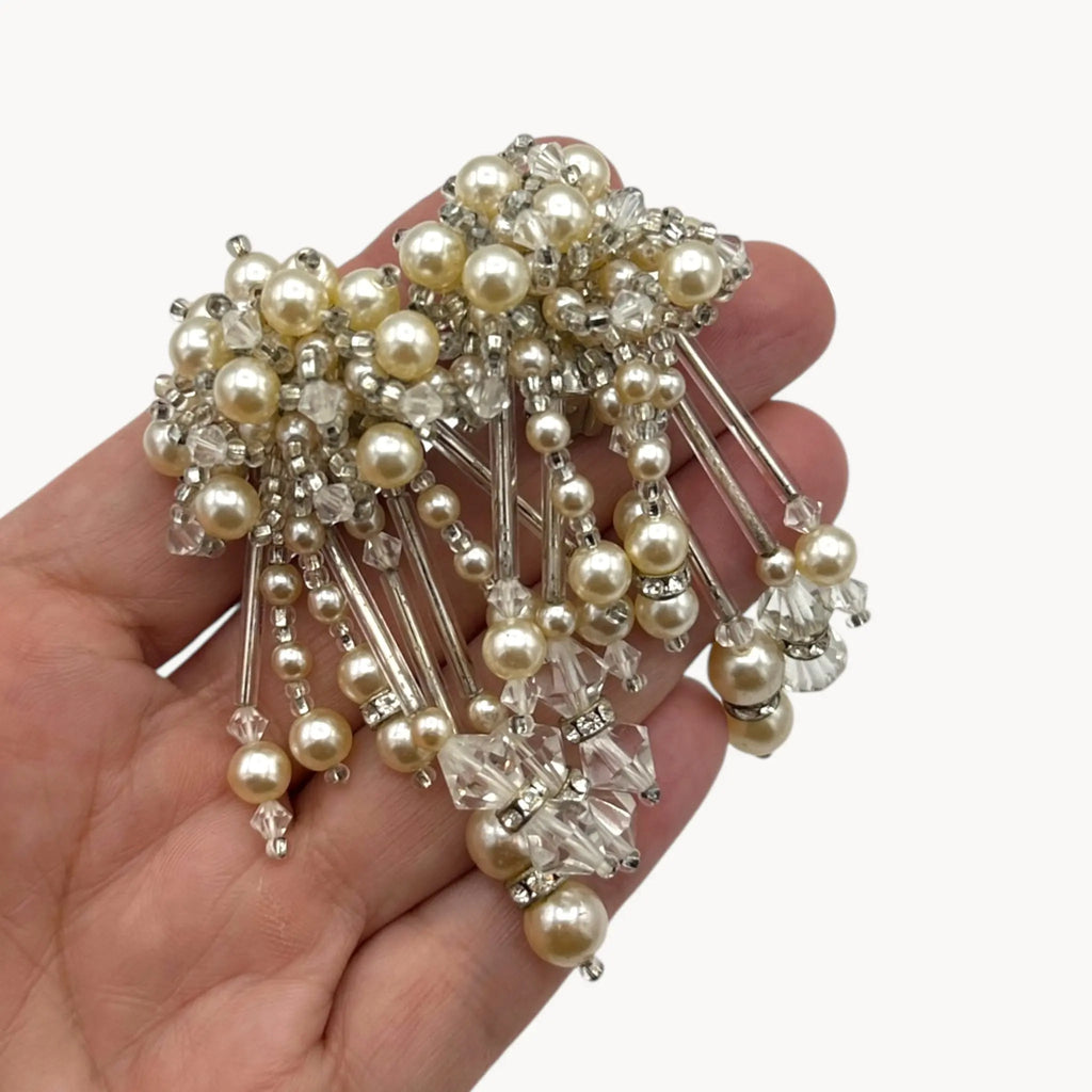 Scale size view on hand of Vintage Lois Ann Pearl & Crystal Beaded Cascade Clip-On Earrings on white background.