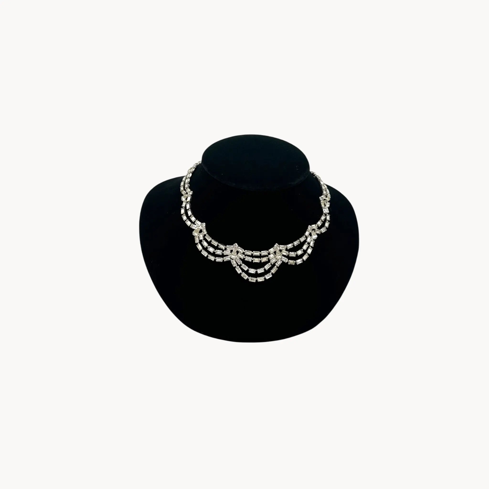 Mid-century draped rhinestone necklace with tiered design displayed on black bust.
