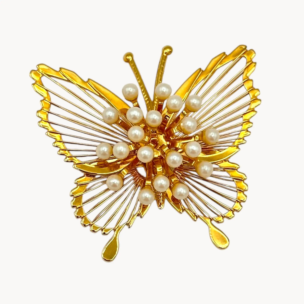 Close up of Vintage Monet butterfly brooch with gold openwork wings and faux pearl accents on white background.