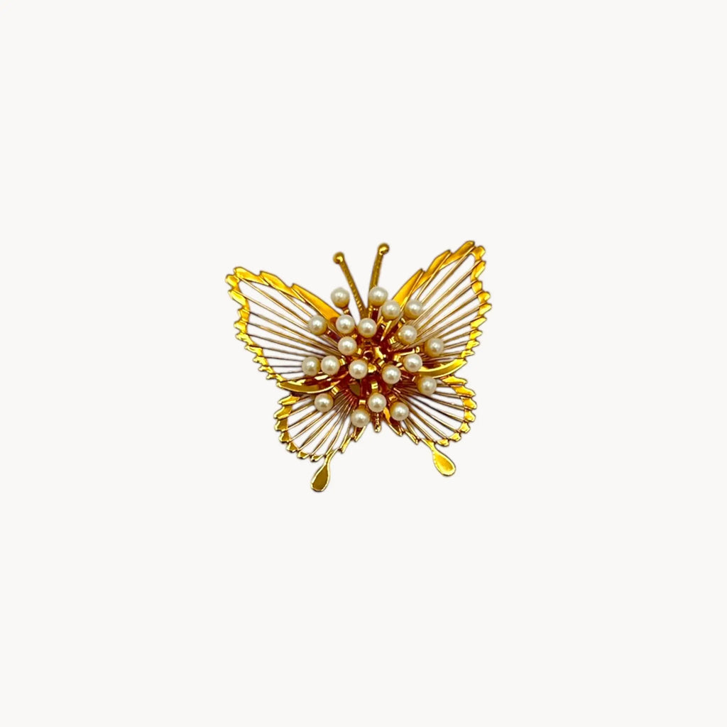 Vintage Monet butterfly brooch with gold openwork wings and faux pearl accents on white background.