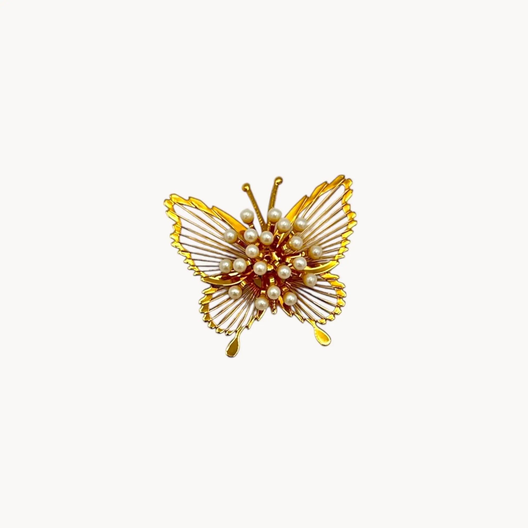 Vintage Monet butterfly brooch with gold openwork wings and faux pearl accents on white background.
