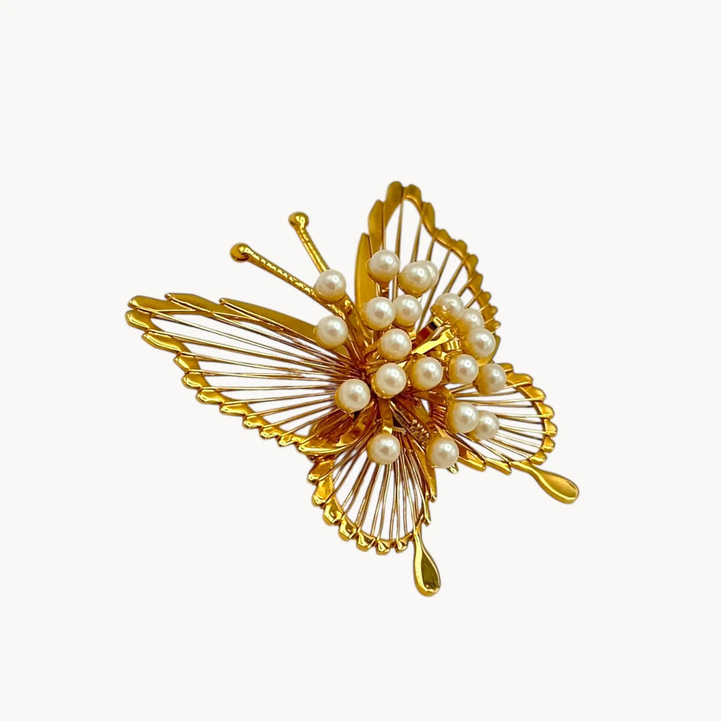 Side view of Vintage Monet butterfly brooch with gold openwork wings and faux pearl accents on white background.