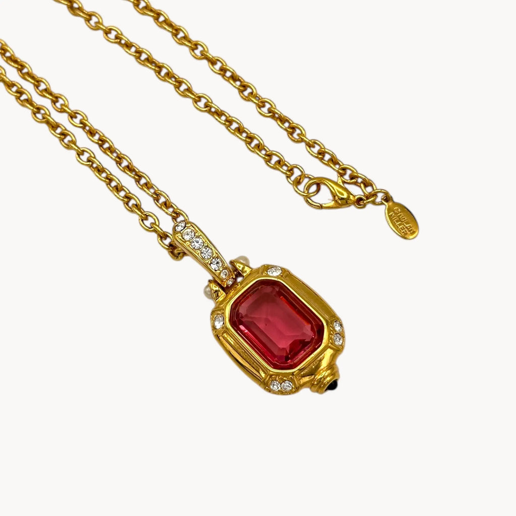 Close up view of Vintage Nolan Miller long gold chain necklace with pink crystal pendant and clear crystal accents, 1980s–1990s bridal jewelry shown on white background.