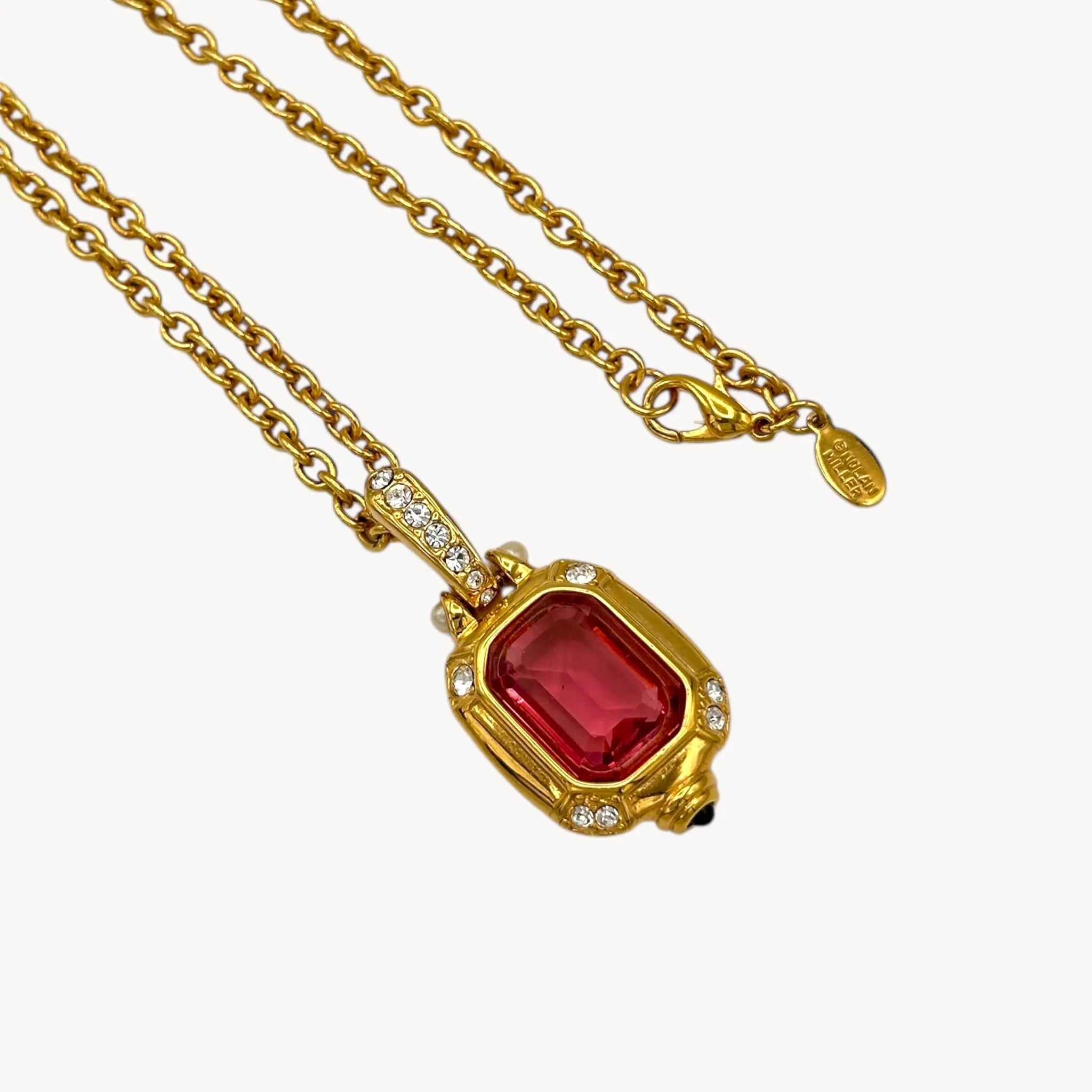 Close up view of Vintage Nolan Miller long gold chain necklace with pink crystal pendant and clear crystal accents, 1980s–1990s bridal jewelry shown on white background.