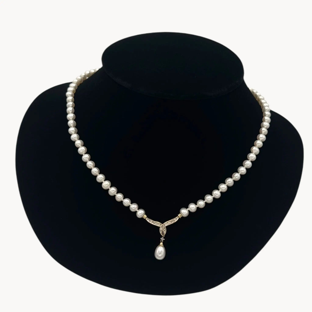 Close up view of Vintage pearl strand necklace with 10K gold and diamond drop pendant, bridal jewelry on black bust.