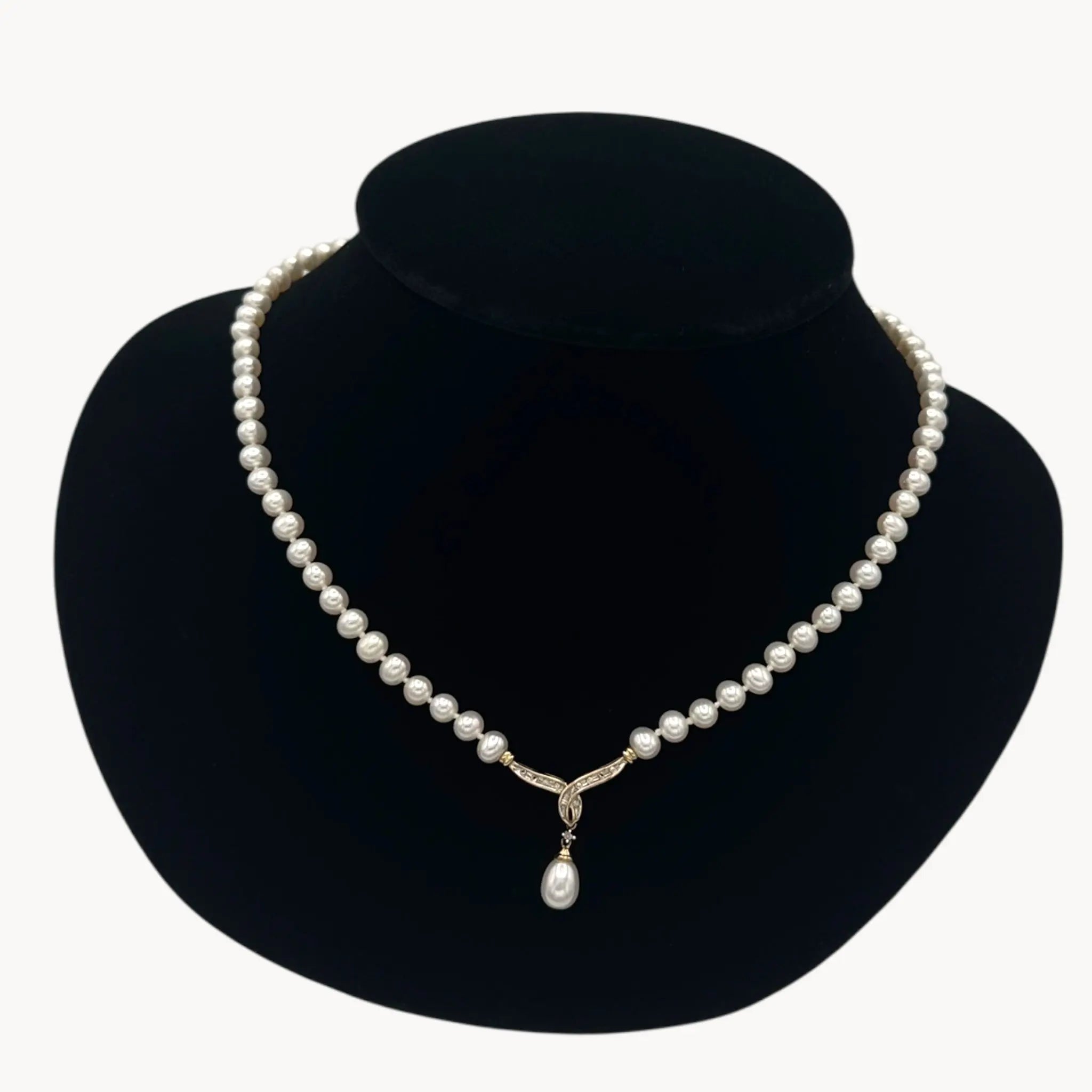 Close up view of Vintage pearl strand necklace with 10K gold and diamond drop pendant, bridal jewelry on black bust.