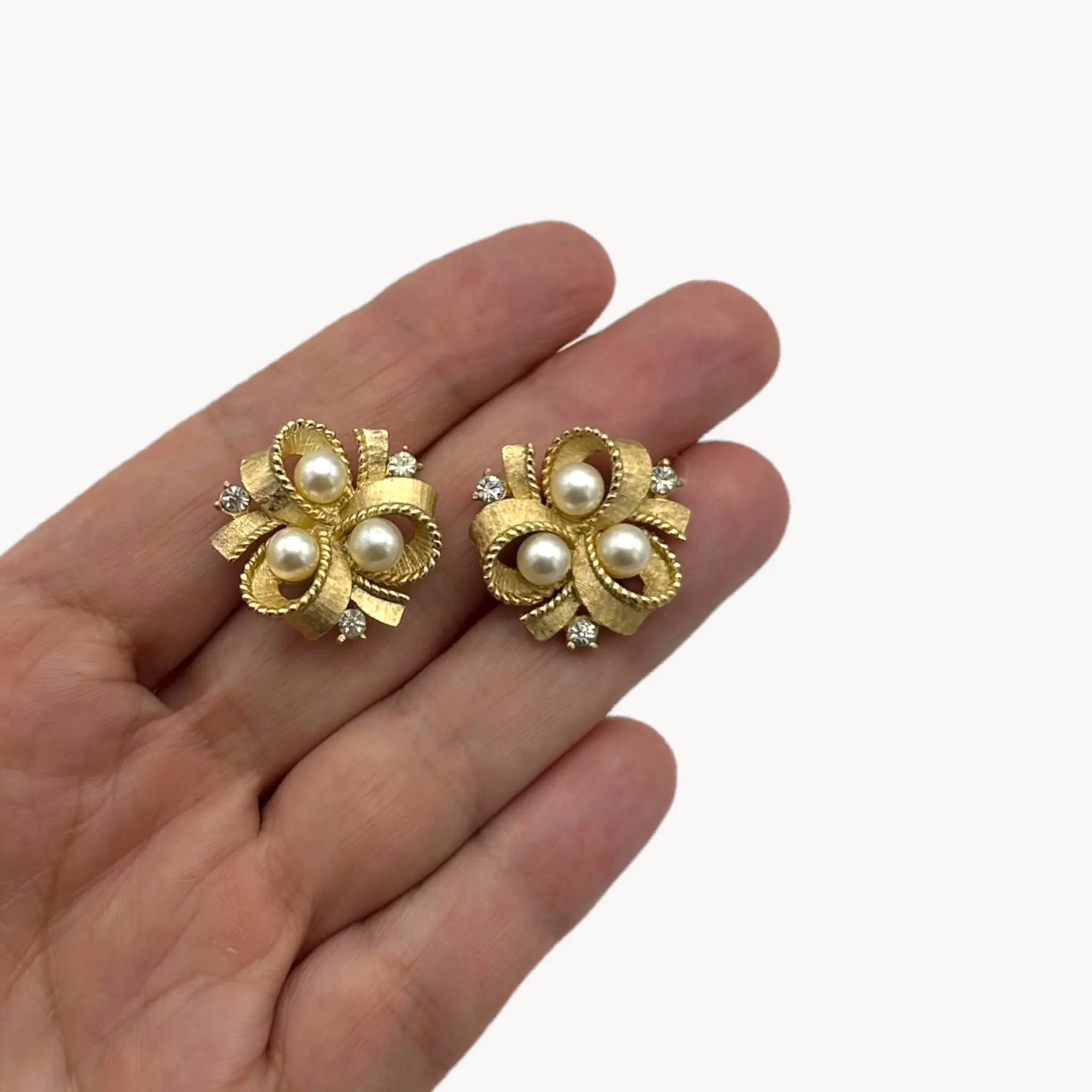 size scale view Vintage Trifari clip-on earrings with gold bow design, faux pearls, and crystal accents, 1960s bridal jewelry.