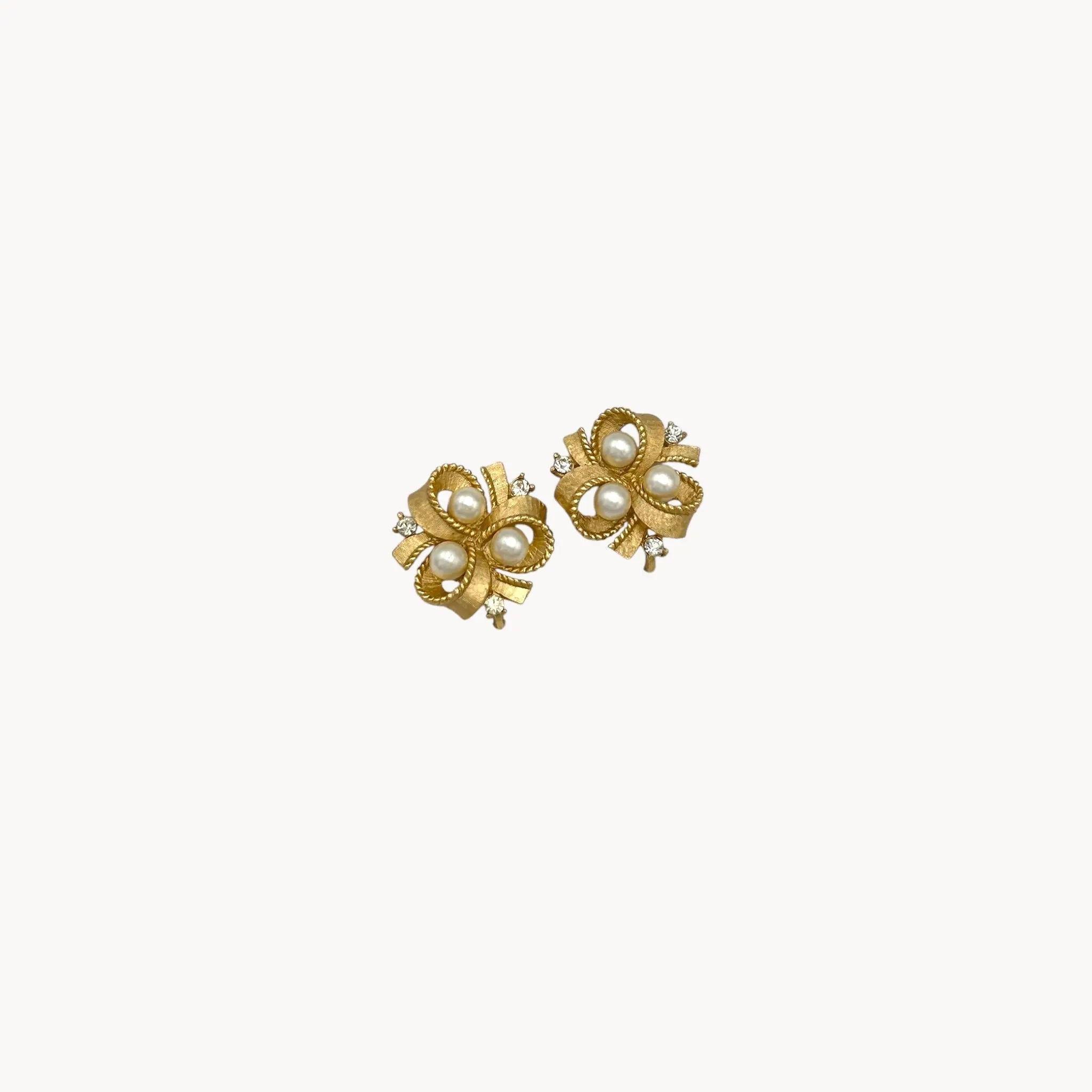 zoom in Vintage Trifari clip-on earrings with gold bow design, faux pearls, and crystal accents, 1960s bridal jewelry.