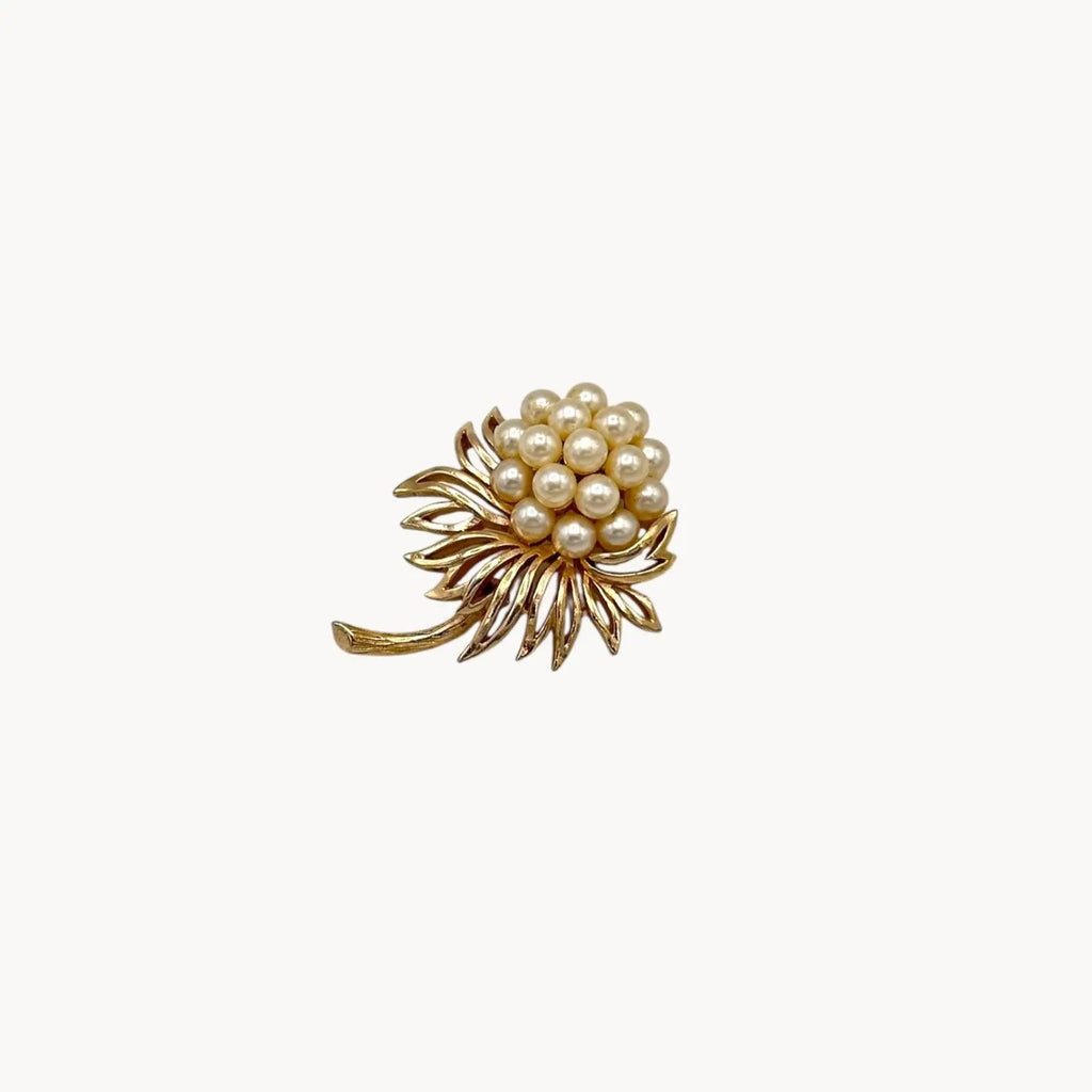 Close up view of Vintage Trifari gold tone flower brooch with faux pearl cluster.