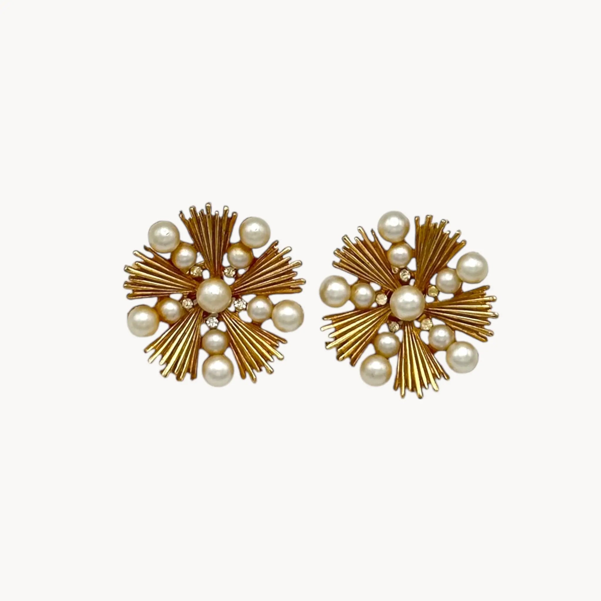 Close up view of Trifari gold starburst clip-on earrings with faux pearls and rhinestones, 1960s jewelry on white background.