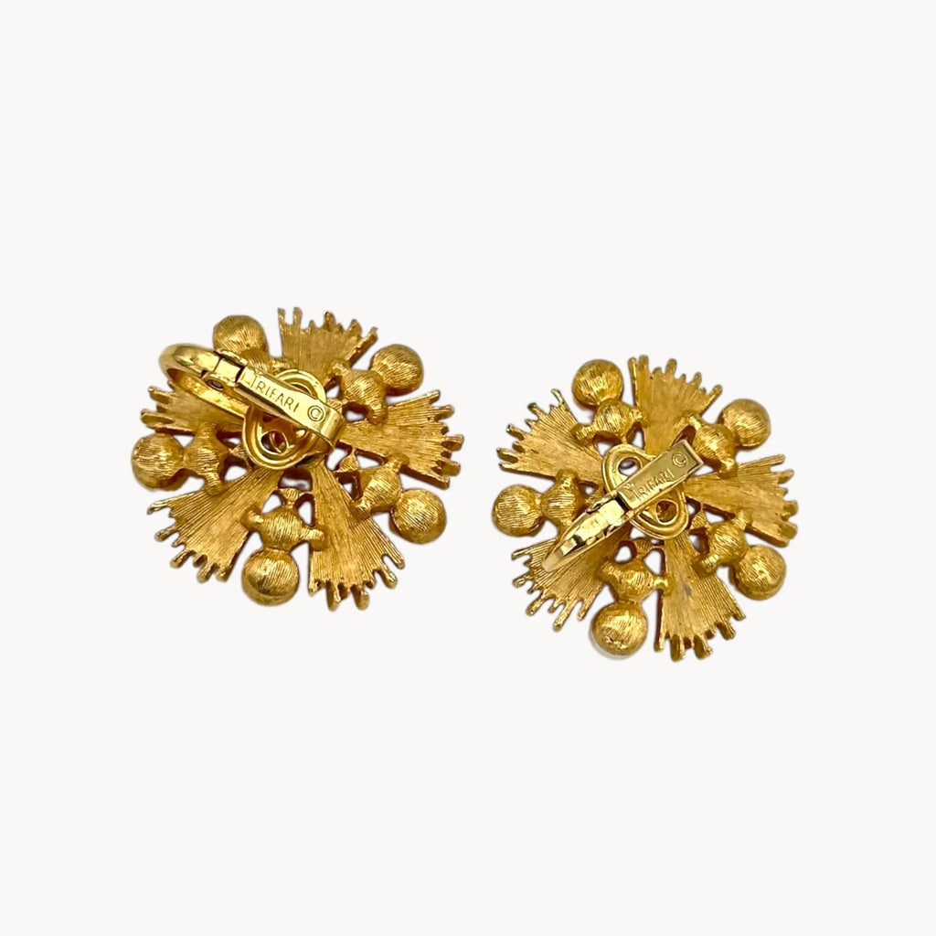 Back view of Trifari gold starburst clip-on earrings with faux pearls and rhinestones, 1960s jewelry on white background.