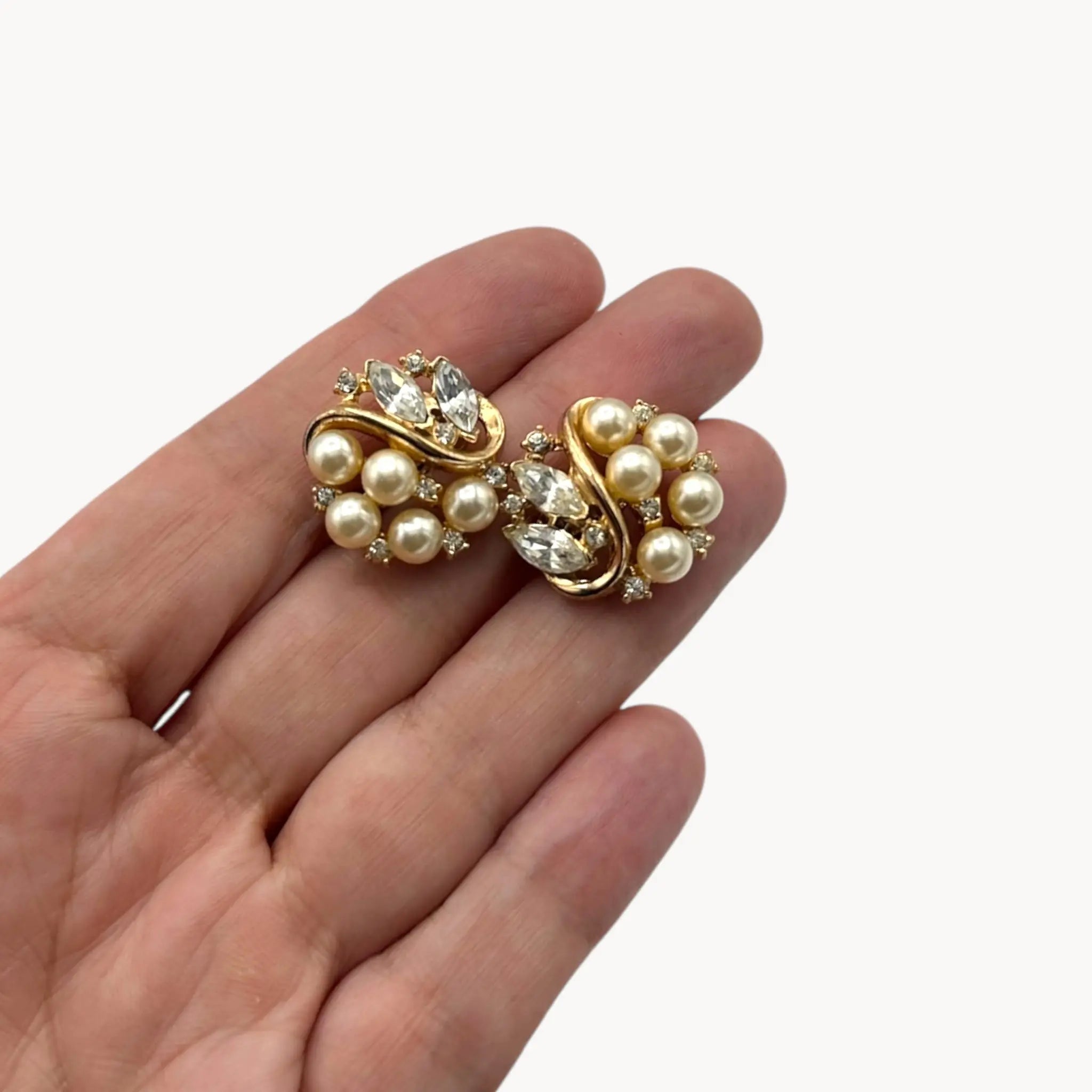 Earrings on hand of the Vintage Trifari brooch with faux pearls, rhinestones, and gold-tone design shown on white background.