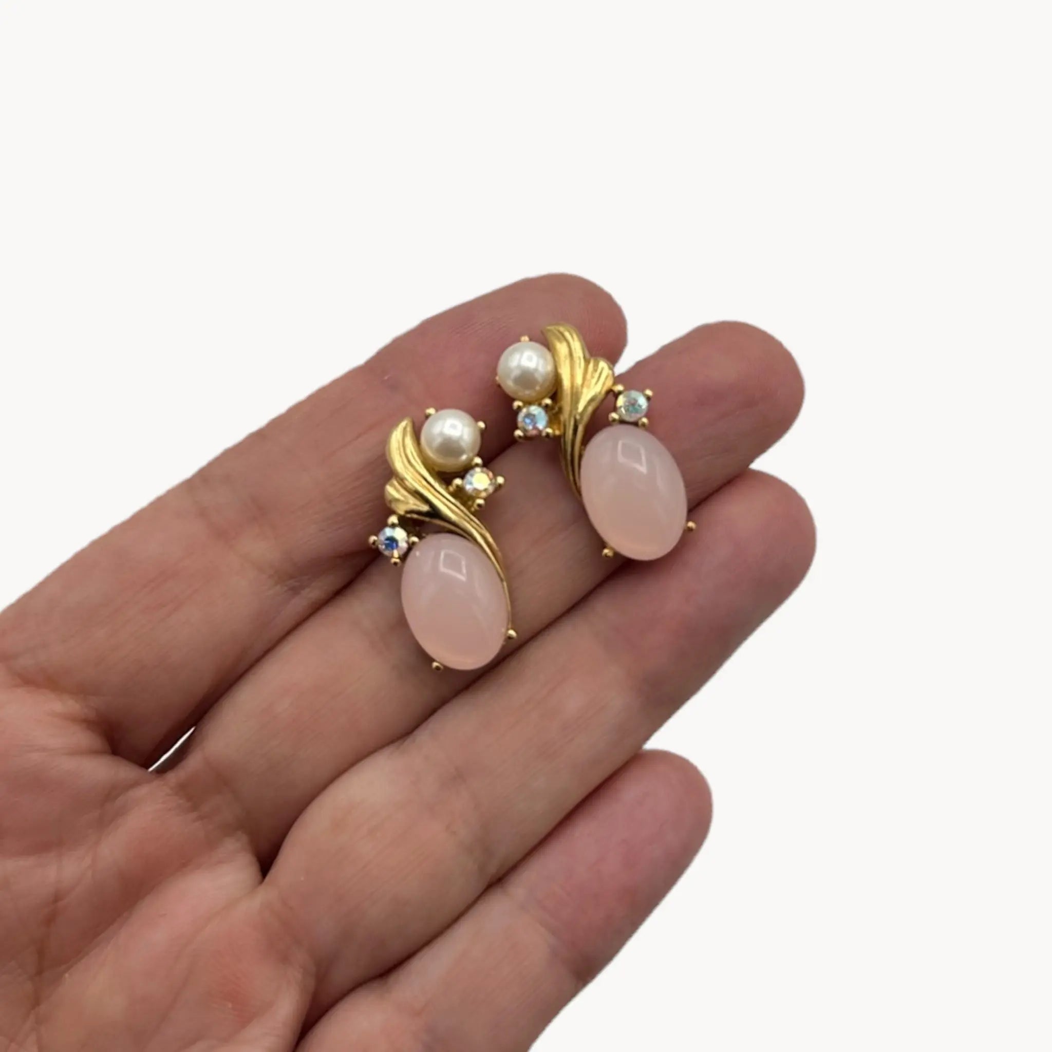 Scale size view on hand of Vintage Trifari pierced earrings with pink cabochon stones, faux pearls, and crystal accents.